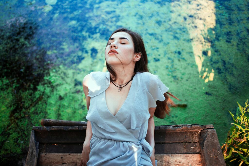 Femeie relaxându-se într-o rochie albastră lângă un râu liniștit, simțind seninătate