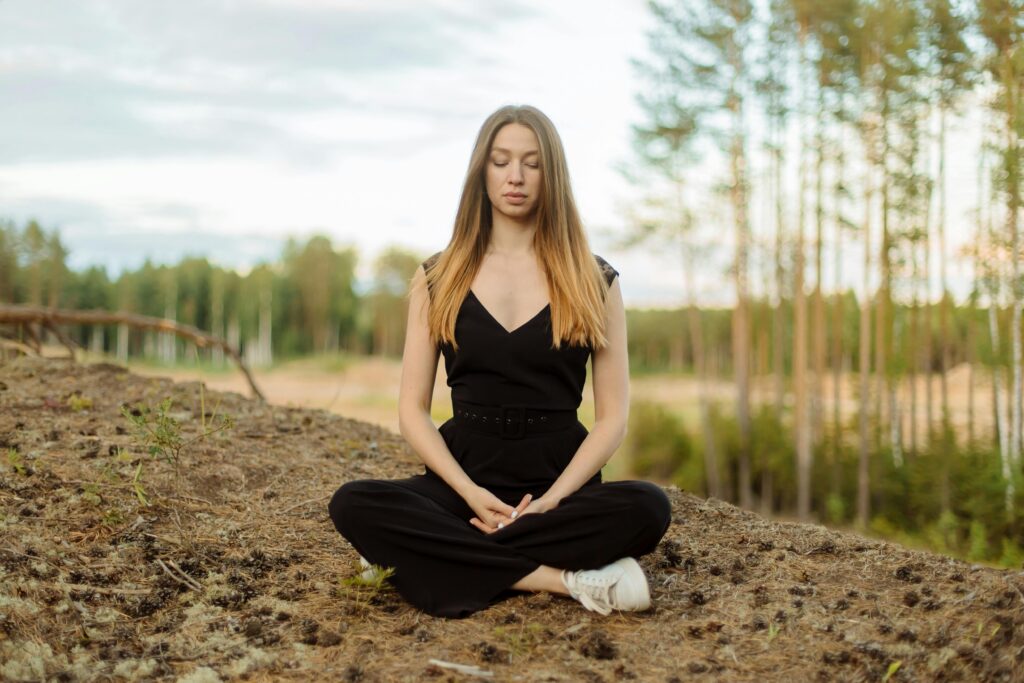 Femeie practicând meditația în natură, un simbol al liniștii și prezenței depline